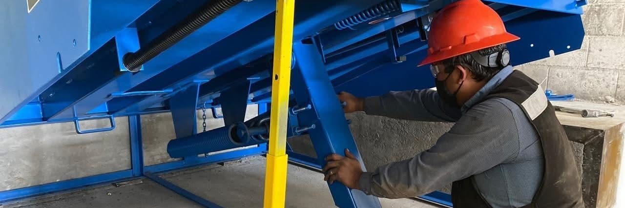 Técnico realizando mantenimiento bajo una rampa niveladora izada y asegurada con puntal de seguridad
